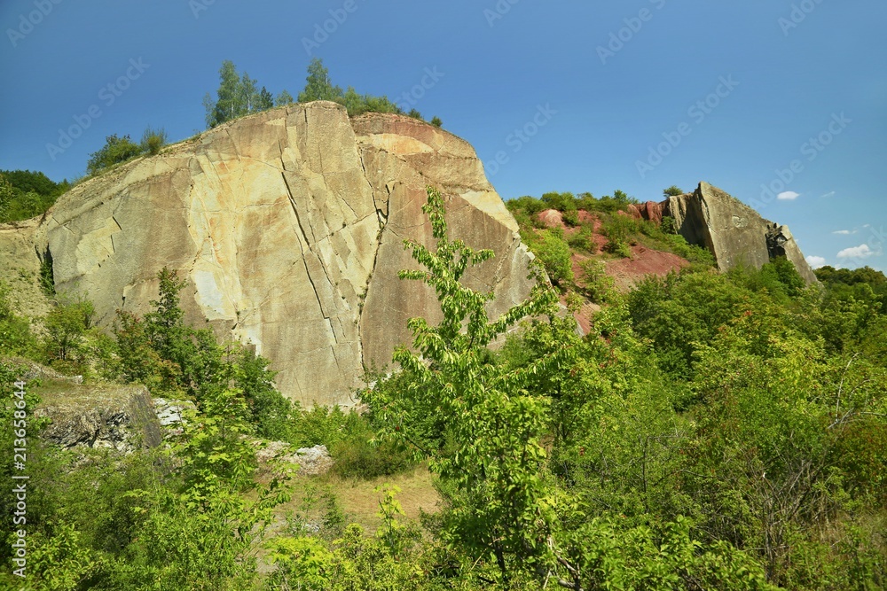 Big yellow and red perpendicular rocks standing in Hlubocepy, Prague, Europe, former limestone quarry, green trees and bushes, sunny summer day, blue sky Big yellow and red perpendicular rocks standing in Hlubocepy, Prague, Europe, former limestone quarry, green trees and bushes, sunny summer day, blue sky