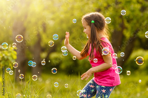 Curly girl catch a soap bubbles. Happy childhood concept.