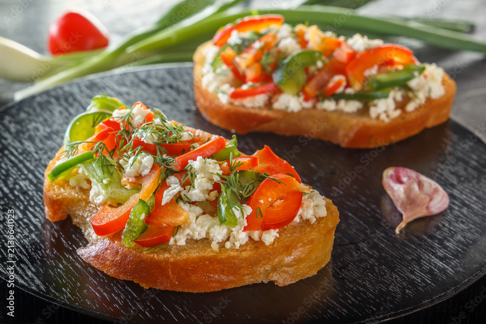 Bruschetta with red sweet pepper and goat cheese on a black table on a background of fresh vegetables. Close-up