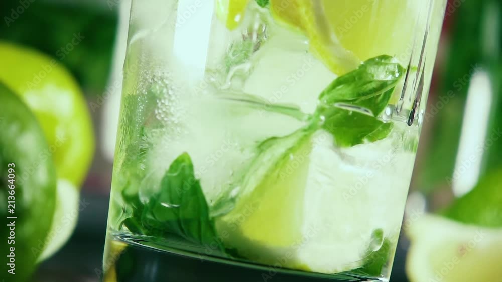 Slow motion vodka pour into a glass of ice with citrus and mint at an angle Slow motion vodka pour into a glass of ice with citrus and mint at an angle