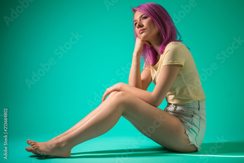 Slender, good-looking female model demonstating her slim leggs and graceful complextion sitting on blue floor in profile photo