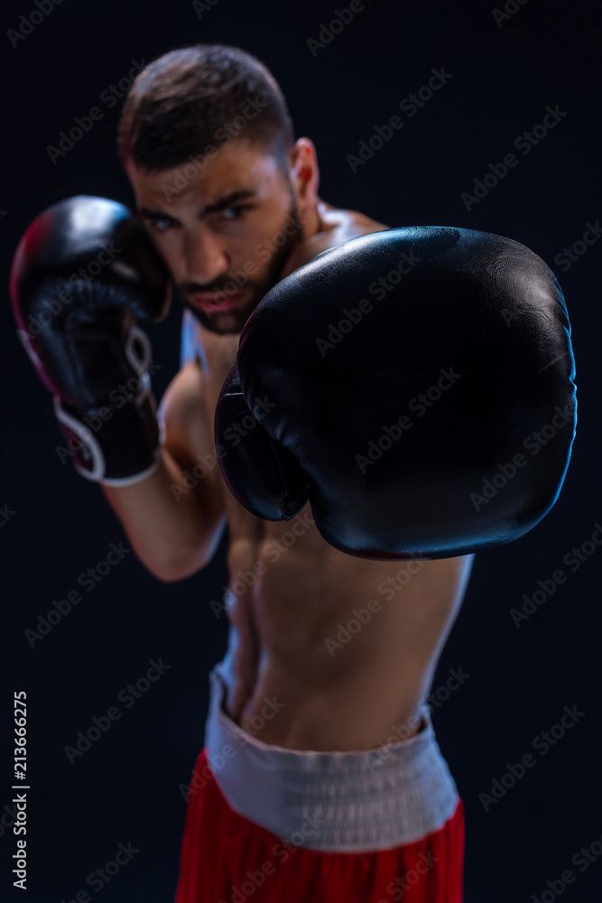 Portrait of tough male boxer posing in boxing stance against black background.