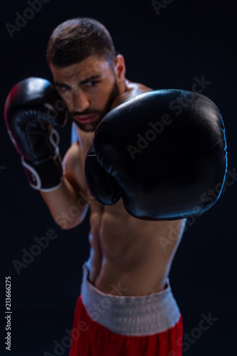 Portrait of tough male boxer posing in boxing stance against black background. © nazarovsergey