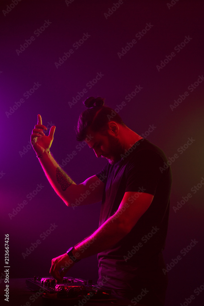 Attractive young DJ playing on turntables with color light effects Attractive young DJ playing on turntables with color light effects