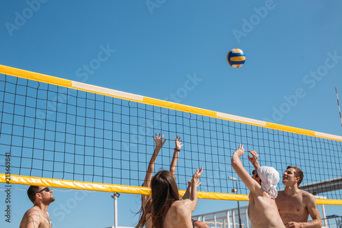 Foto Rear view of unrecognizable caucasian males and females playing amateur beach valleyball, ball flying in the air against blue sky background