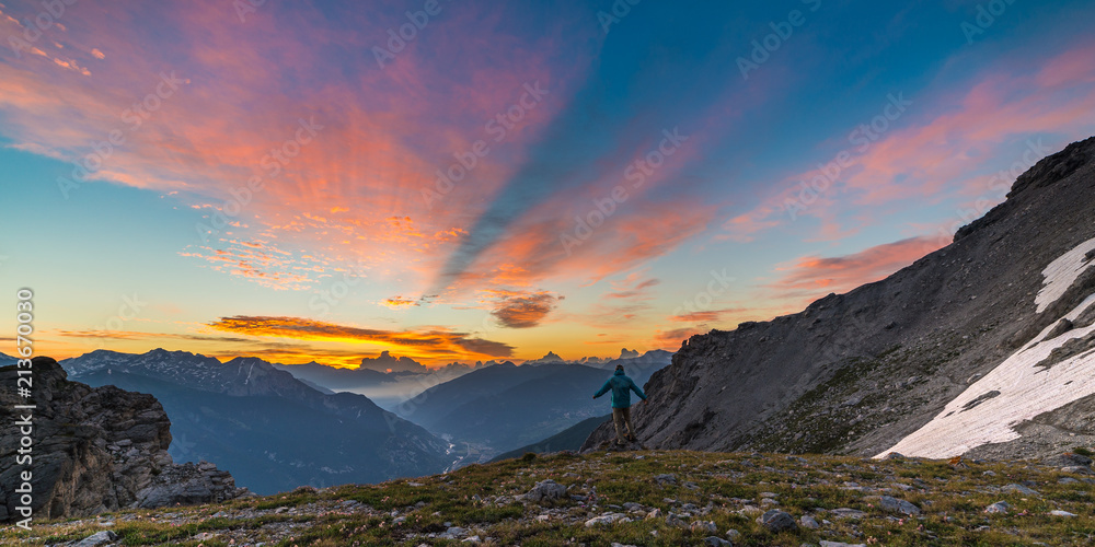 Man standing on mountain top raising arms, sunrise light colorful sky scenis landscape, conquering success leader concept.