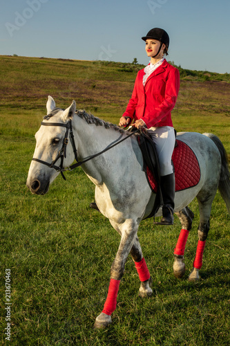 Young woman rider, wearing red redingote and white breeches, with her horse in evening sunset light. photo