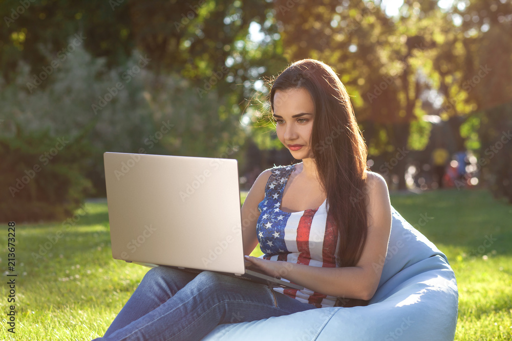 Young cute girl with laptop, sit on bean bag in garden or park, on green grass. Online shopping concept Young cute girl with laptop, sit on bean bag in garden or park, on green grass. Online shopping concept
