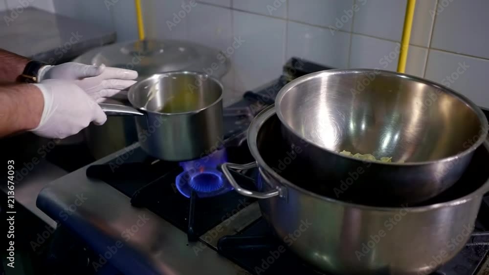 confectioner is melting butter oil in a metal bowl, holding it over fire of gas cooker on a kitchen, close-up confectioner is melting butter oil in a metal bowl, holding it over fire of gas cooker on a kitchen, close-up