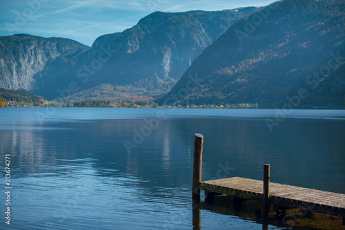 Scenic view of a calm water lake with wooden pier surrounded by mountains in Hallstat, Austria