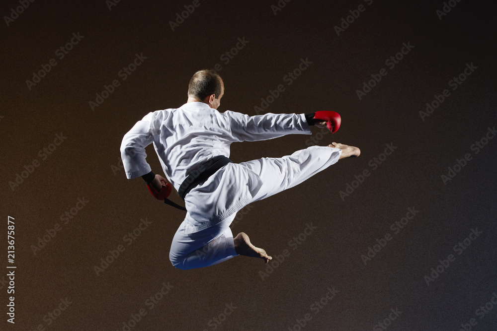 With a black belt, an athlete trains a kick in the jump to the side