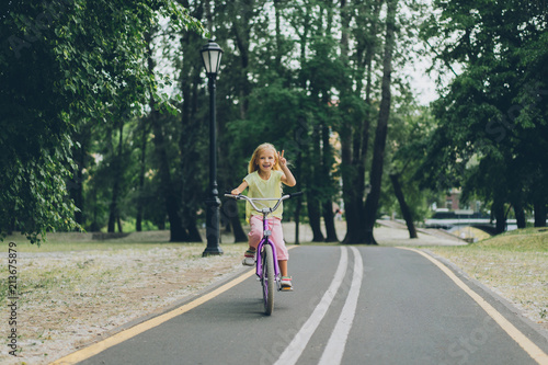 Wallpaper Mural little child showing peace sign while riding bicycle on road in park on summer day Torontodigital.ca
