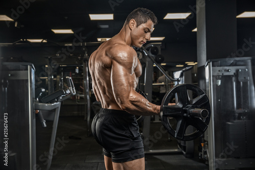 A handsome male athlete is a bodybuilder, weightlifter, doing exercises for the development of triceps muscles, exercising on a simulator in a modern gym. 