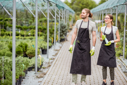 Young couple of workers in uniform supervising plants in the greenhouse