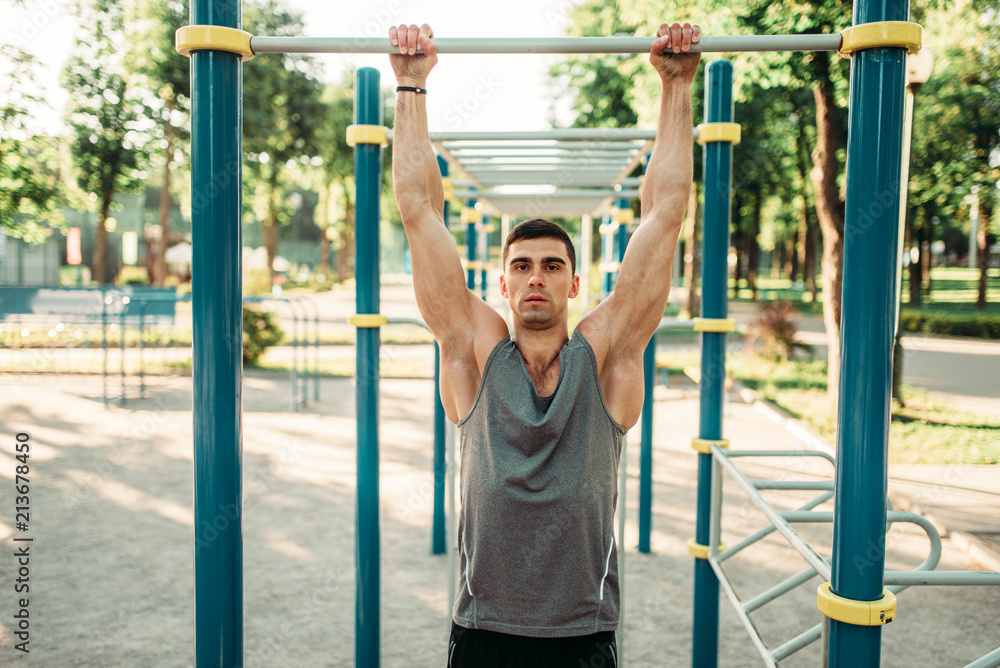 Fototapeta premium Athlete doing exercise on horizontal bar outdoor