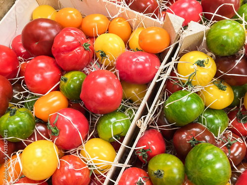 Fresh organic cultured tomatoes in different colors and flavors laying in wooden boxes at farmers market.