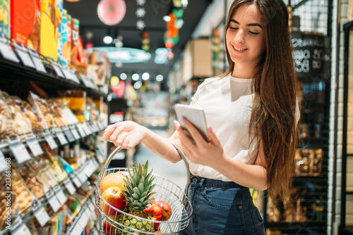 Fotografiet Female customer uses mobile phone in supermarket