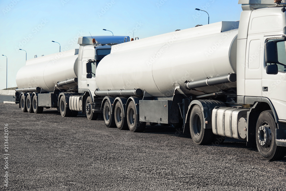 two white tank trucks on the road, clear and blank space on the cistern side