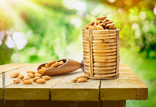 Almonds in cane basket and wooden scoop on wooden table in morning sunlight outdoor photo