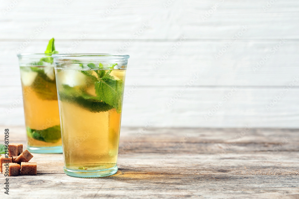 Glasses with aromatic mint tea, fresh leaves and sugar cubes on wooden table Glasses with aromatic mint tea, fresh leaves and sugar cubes on wooden table