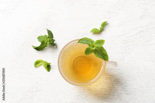 Cup with hot aromatic mint tea and fresh leaves on table, top view