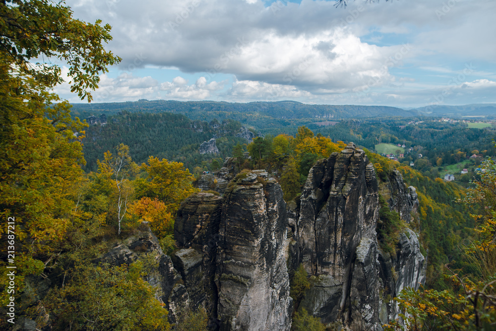 Scenic autumn landscape of rocky mountains and forest with colorful trees in Saxon Switzerland National Park on cloudy day. Germany