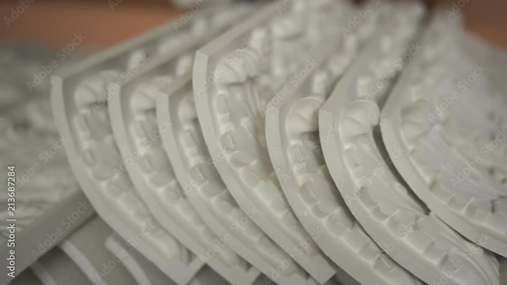 White plaster decorations are laying on table in light workshop, gypsum artistic ornaments with beautiful antique patterns are prepared for restoration of cultural heritage. Concept: restoring White plaster decorations are laying on table in light workshop, gypsum artistic ornaments with beautiful antique patterns are prepared for restoration of cultural heritage. Concept: restoring