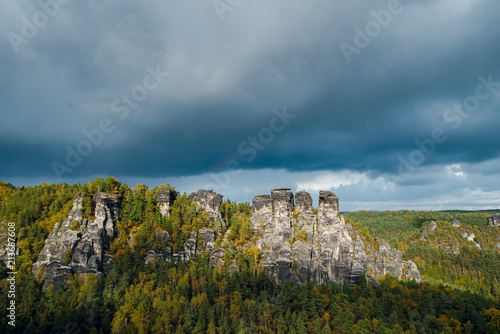Wonderful Autumn landscape of rocky mountains and forest with colorful trees in Saxon Switzerland National Park on cloudy day. Before the rain and storm. Germany