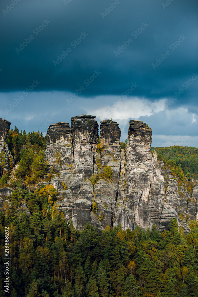 Gloomy Autumn landscape of rocky mountains and forest with colorful trees in Saxon Switzerland National Park on cloudy day. Before the rain and storm. Germany