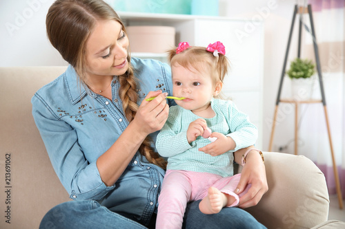 Caring mother feeding her cute little baby with healthy food at home