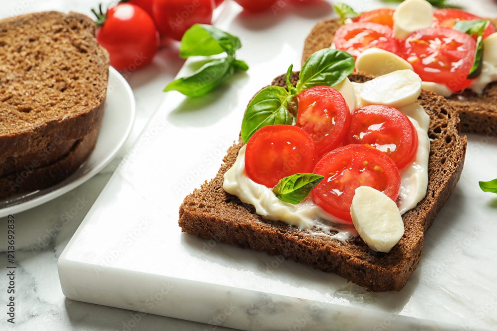 Toast bread with cherry tomatoes and mozzarella cheese on marble board, closeup