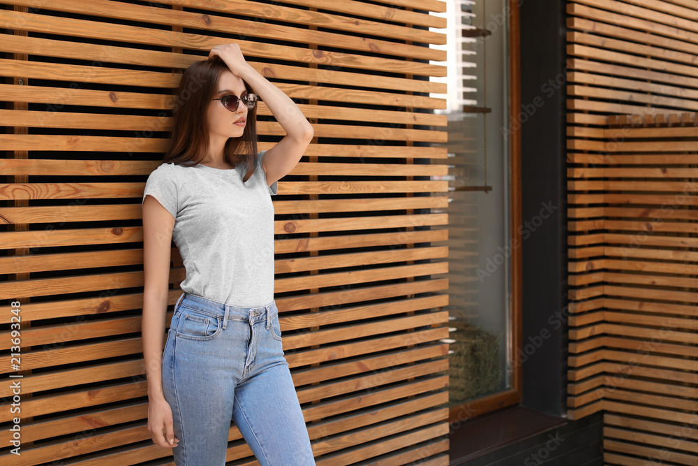 Young woman wearing gray t-shirt near wooden wall on street. Urban style