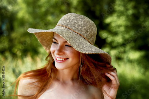 A sophisticated red-haired girl in a simple linen dress, in a light wide-brimmed hat. Model look. Natural beauty. Artistic portrait