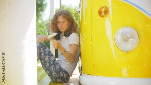 young woman outdoors by yellow vagon car listening music in headphones using smartphone - relaxing, enjoying, concept of technology and travel photo