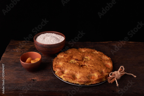 On a dark wooden table, fashionable bakeries, a bowl with flour, apricot cake and tools stand on table photo