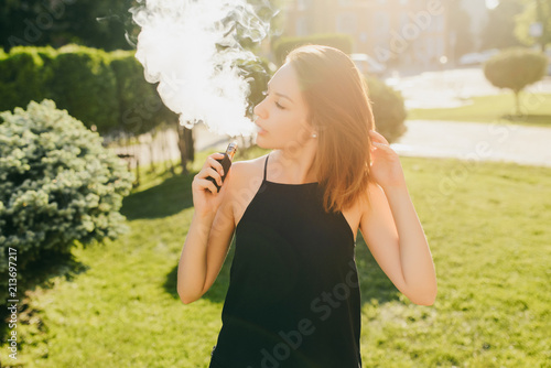Fashionable young charming girl with an electronic cigarette  smoking outdoors  vapor.