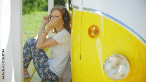 young woman outdoors by yellow vagon car listening music in headphones using smartphone - relaxing, enjoying, concept of technology and travel photo