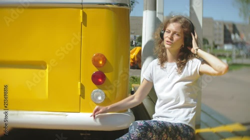 young woman outdoors by yellow vagon car listening music in headphones using smartphone - relaxing, enjoying, concept of technology and travel photo