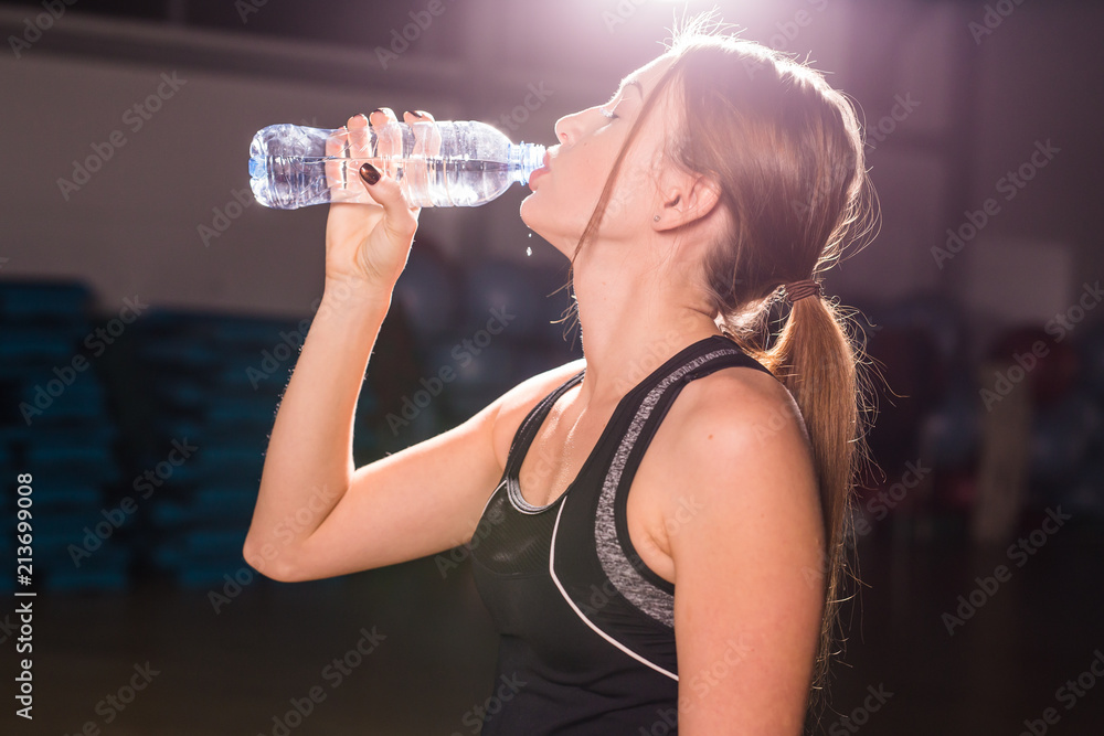 Fitness young woman drinking water from bottle. Muscular young female at gym taking a break from workout. Fitness young woman drinking water from bottle. Muscular young female at gym taking a break from workout.