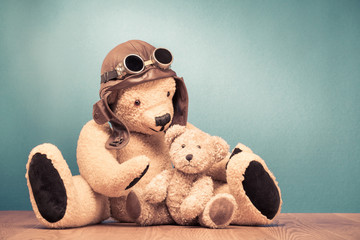 Retro Teddy Bear toy in leather pilot's hat and vintage goggles playing with baby front mint green wall background. Old style filtered photo