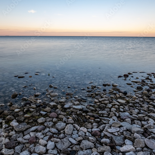 dramatic sunrise over the baltic sea with rocky beach and trees on the shore © Martins Vanags