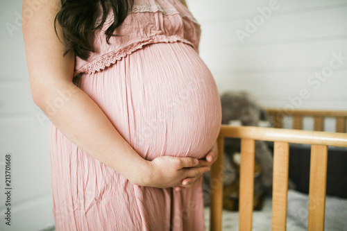 Midsection of pregnant woman touching belly while standing by crib at home photo