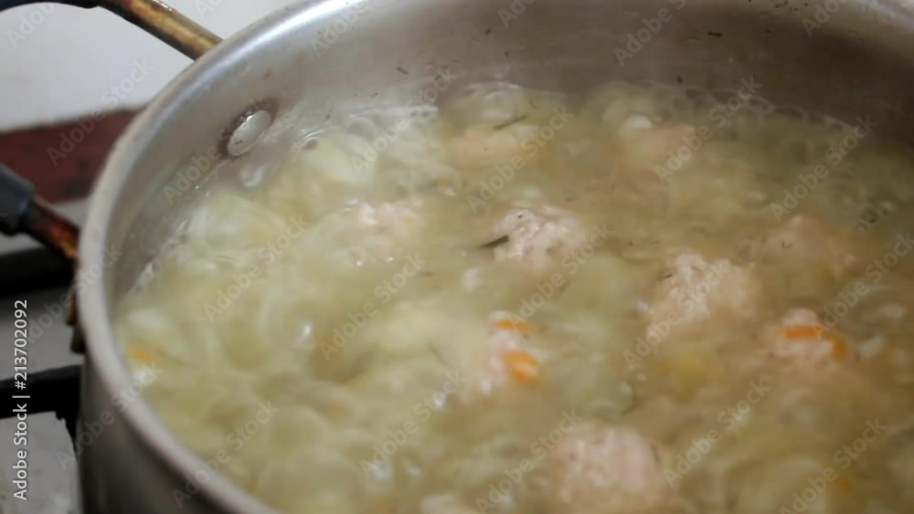 The female hand opens the lid on the pan and stirs the boiling soup with the meatballs The female hand opens the lid on the pan and stirs the boiling soup with the meatballs