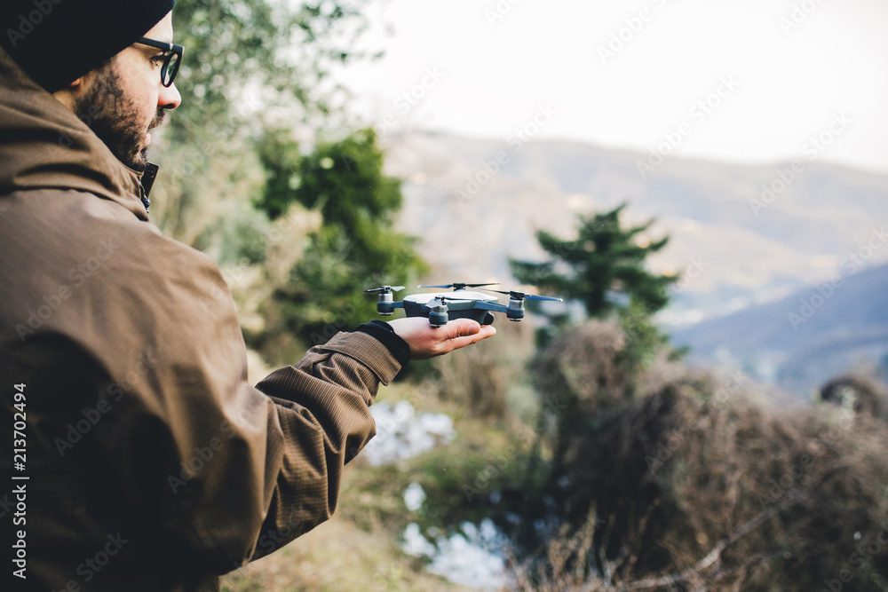 Side view of male hiker holding quadcopter while standing on mountain in forest Side view of male hiker holding quadcopter while standing on mountain in forest