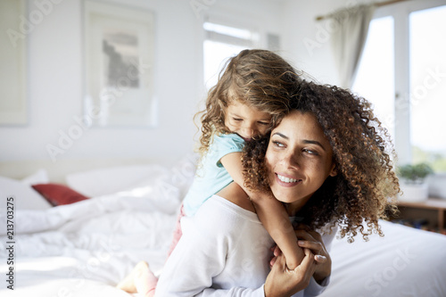 Happy daughter embracing mother sitting on bed at home photo