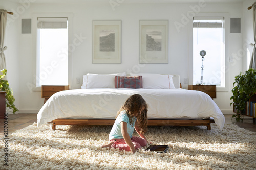 Side view of girl using tablet computer while sitting on rug in bedroom photo