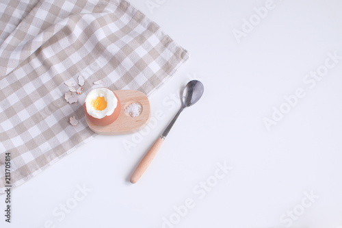 Served table for breakfast boild egg in wooden egg cup with salt spoon and checkered napkin White background Top view Minimalism Copy space