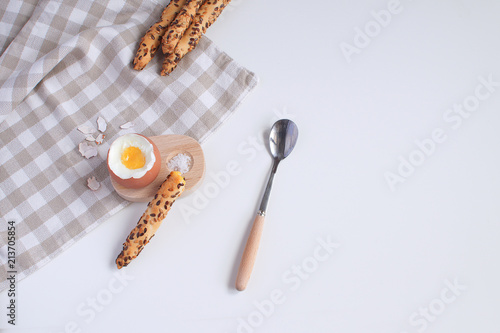Served breakfast boiled egg in wooden egg cup with breadsticks salt spoon and checkered napkin White background Top view Minimalism Copy space