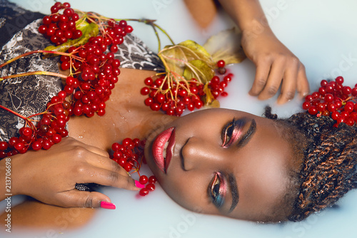 Glamorous African woman with bright make-up in milk with red berries top view close-up. The