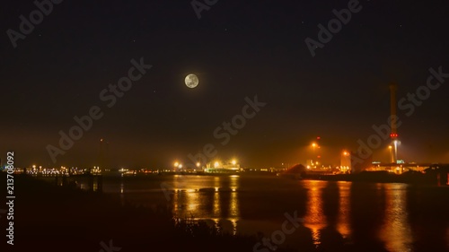 View of cargo port at night . View of the loading in the sea port . Cargo area on night time with reflections on water . eclipse of the moon 